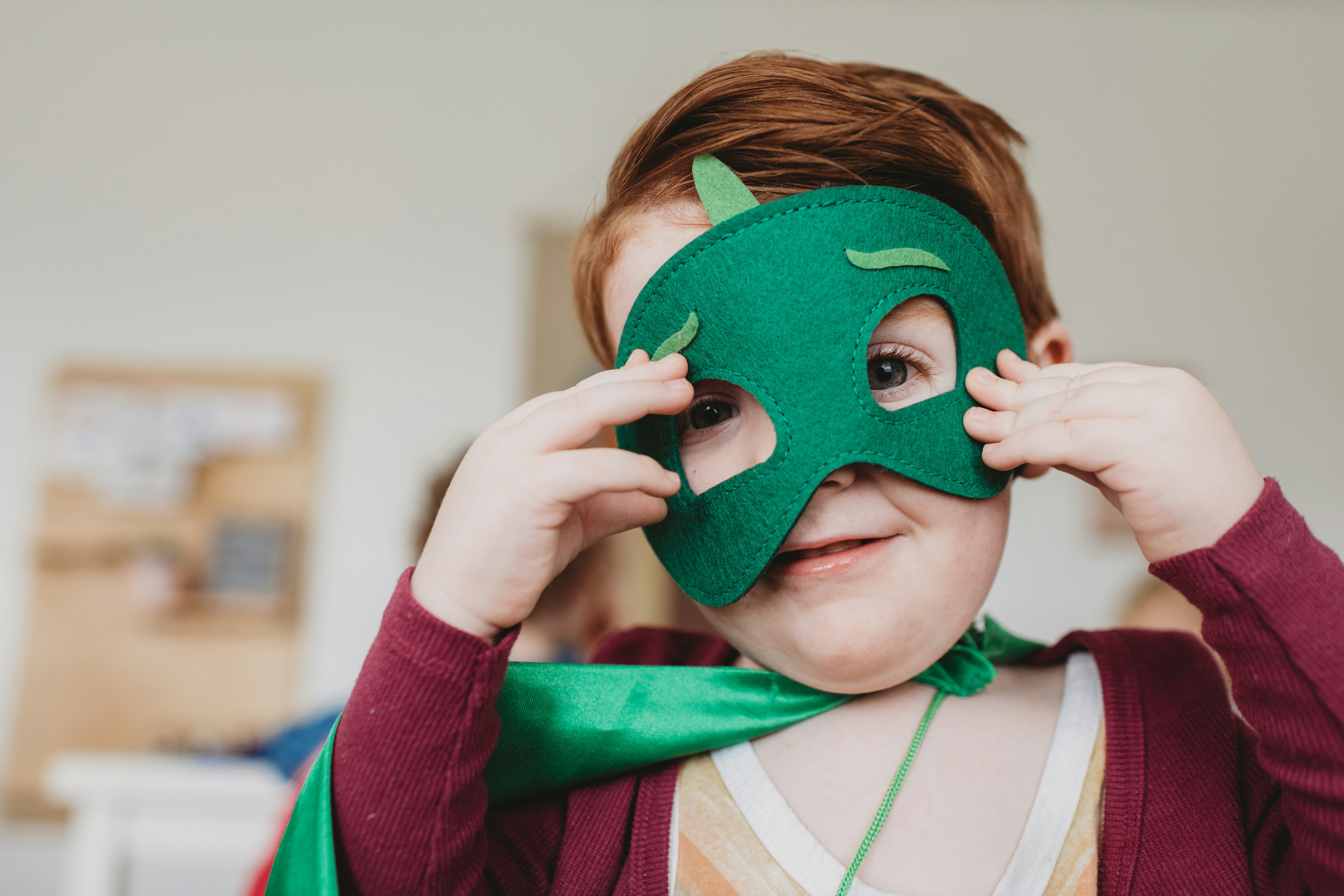 Happy child wearing green superhero mask during therapy session, representing empowerment and confidence building