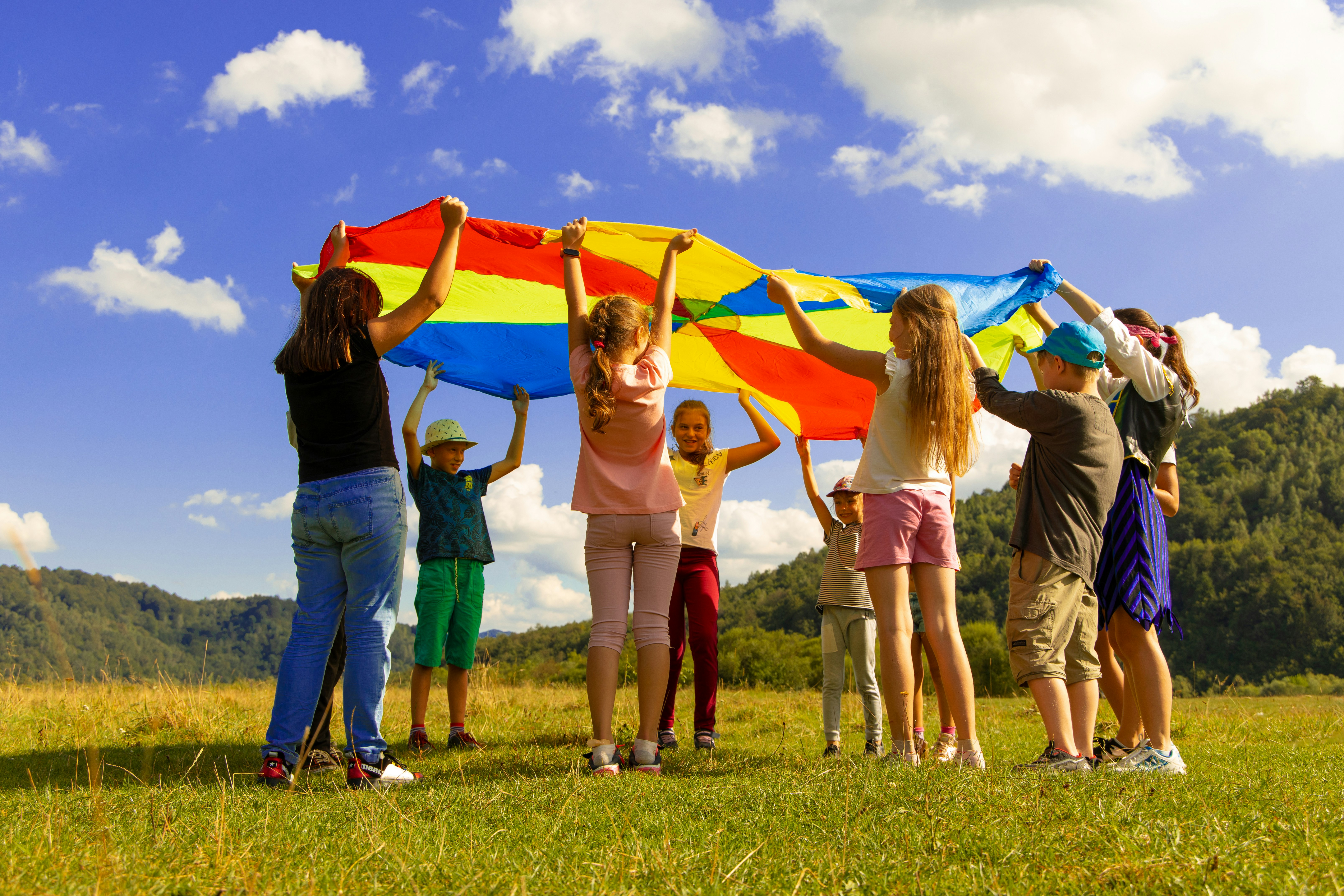 Diverse group of children playing together with a colorful parachute outdoors, demonstrating teamwork, cooperation, and community engagement in a joyful group activity